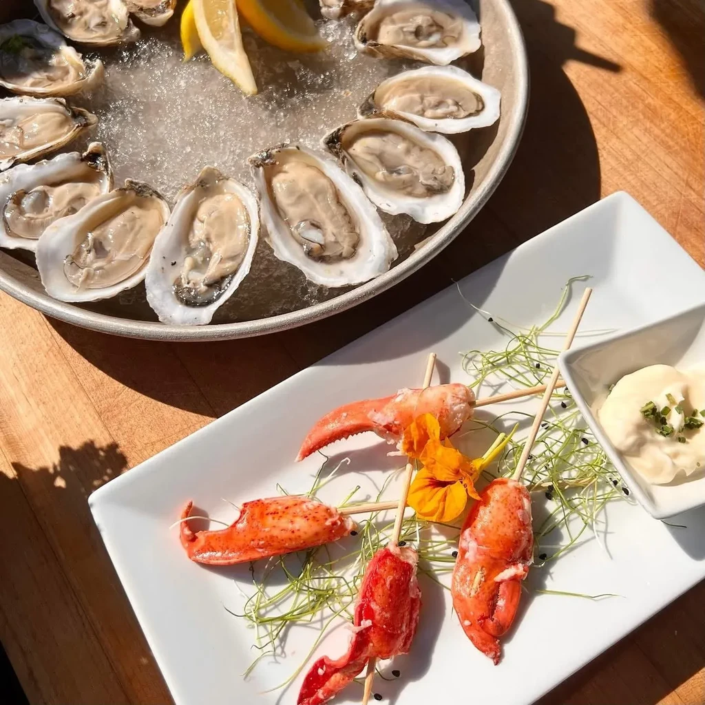 Fresh oysters on ice, cooked lobster, and sauce on a wooden table.