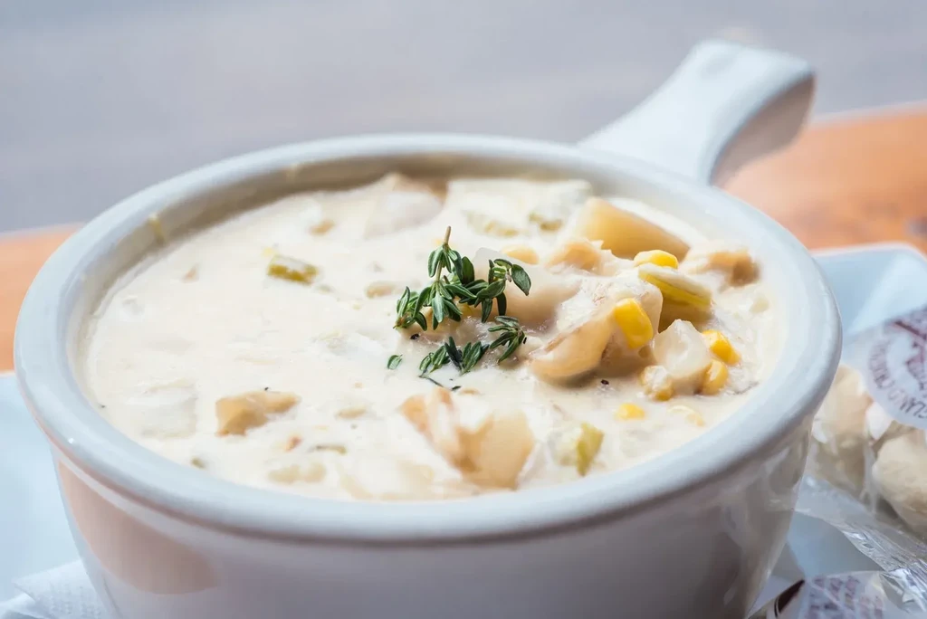 Steaming creamy chowder with corn, potatoes, thyme, and oyster crackers.