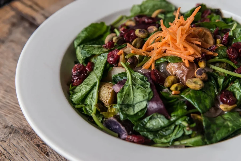 Colorful salad with roasted vegetables, greens, cranberries, pistachios, and carrots.