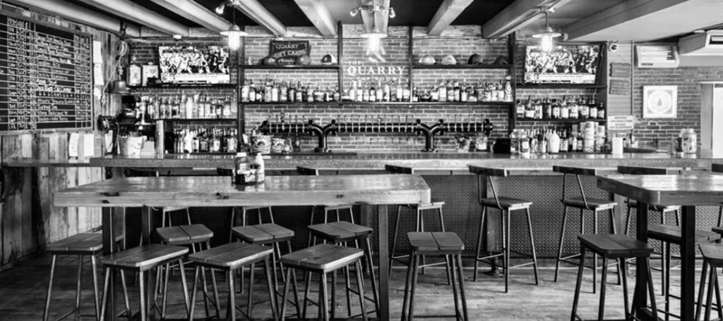 Black and white, rustic-industrial bar with beer taps and alcohol bottles.