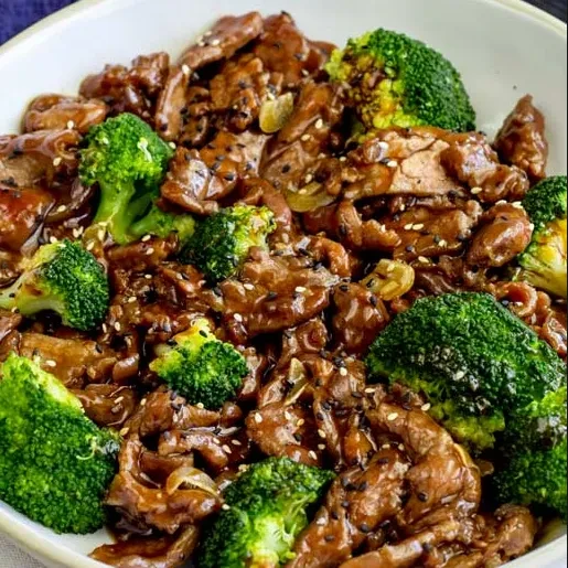 Close-up beef and broccoli stir-fry with sesame seeds in white bowl.