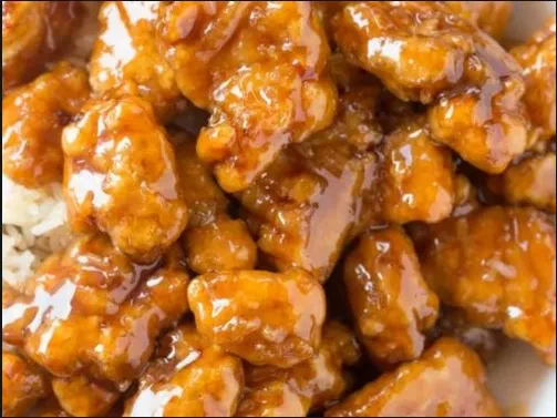Close-up of breaded chicken in glossy amber-orange sauce with white rice.