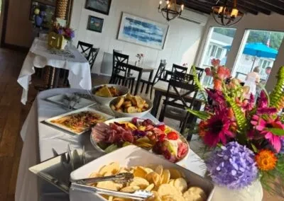 Indoor event buffet with food, vibrant flowers, and a waterfront view.