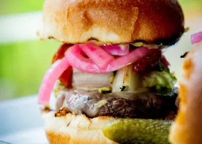 Char-grilled hamburger with melted cheese, pickled red onions, and a pickle.