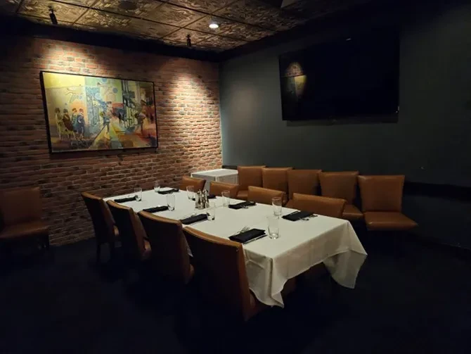 Dimly lit private dining room with set table, abstract art, and TV.
