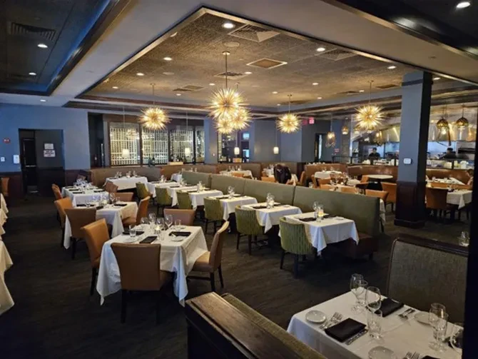 Upscale restaurant dining room with tables, booths, starburst chandeliers, and open kitchen.