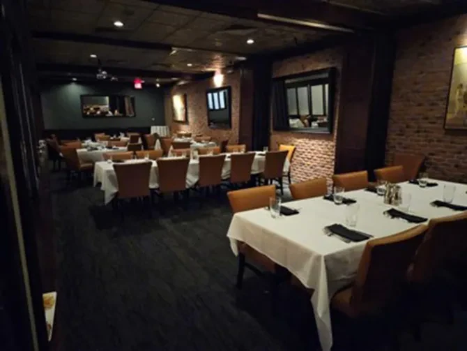 Dimly lit restaurant dining area with set tables, brick walls, and wood floor.
