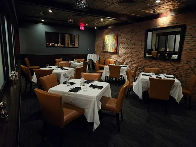 Restaurant dining room: white tables, cognac chairs, brick wall.