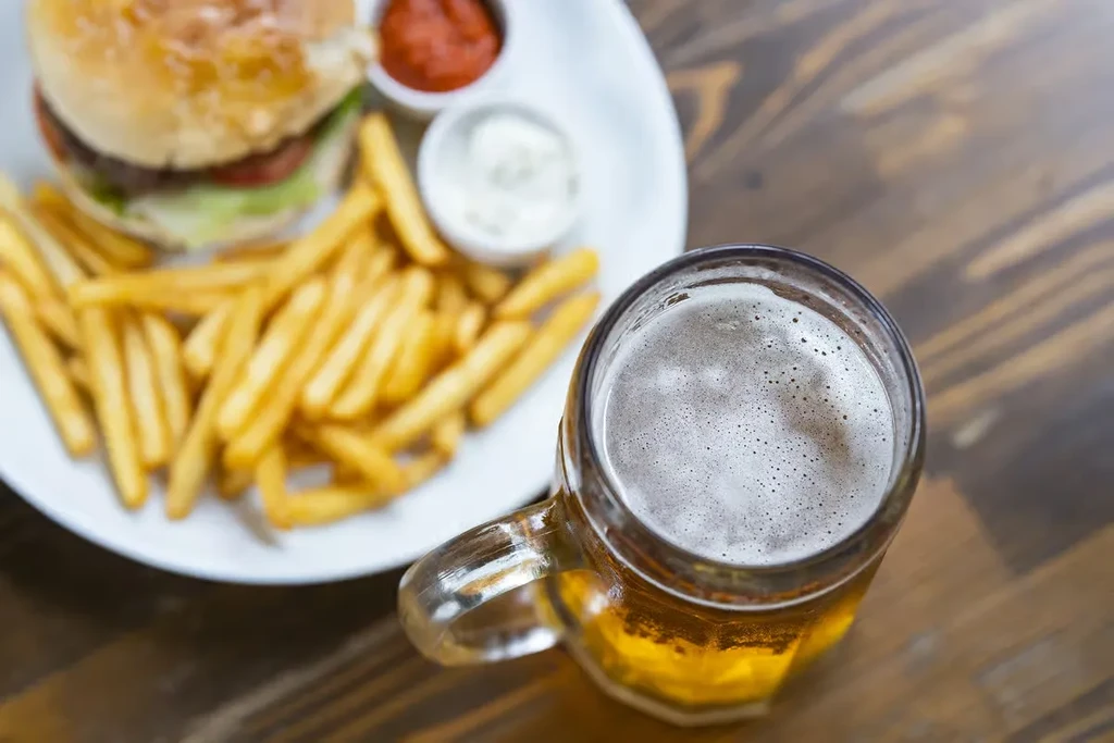 Frosty beer mug, hamburger, and fries on a dark wooden table.