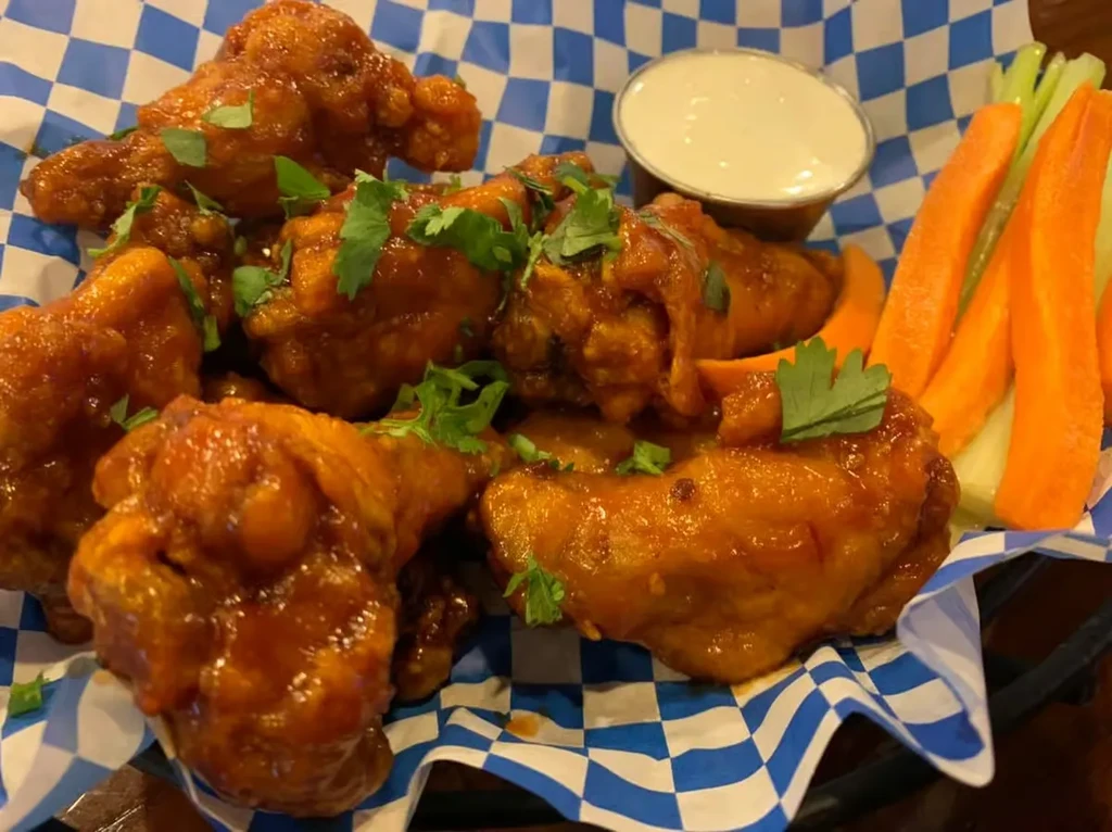 Basket of buffalo chicken wings, dipping sauce, celery, and carrots.