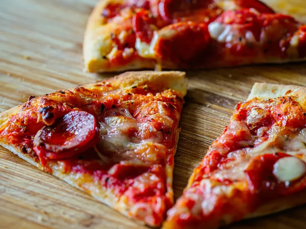 Three freshly baked pepperoni pizza slices on a light wooden board.