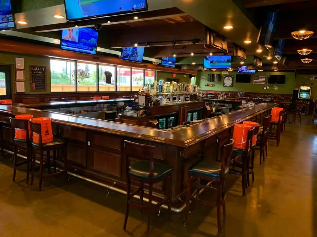 Large U-shaped wooden bar in empty sports pub with many TVs.