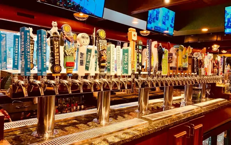 Dozens of colorful craft beer taps on a shiny bar.