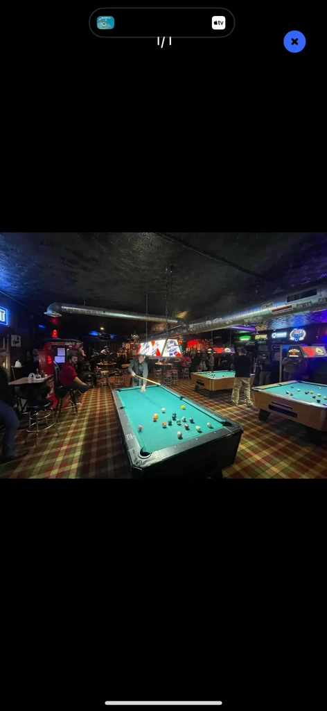 Dimly lit bar, people playing pool, red and green checkered floor.