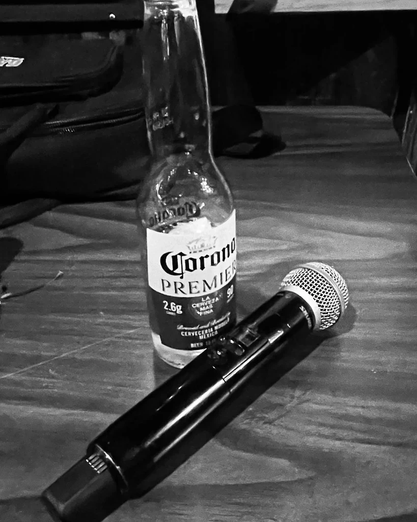 Black and white photo: Corona Premier bottle and microphone on wooden table.