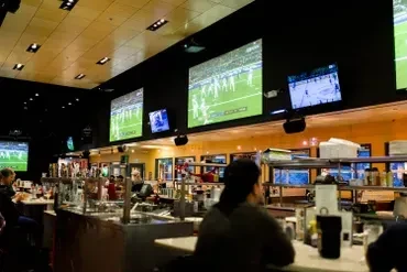 Dim sports bar interior with TVs showing games above a bar.