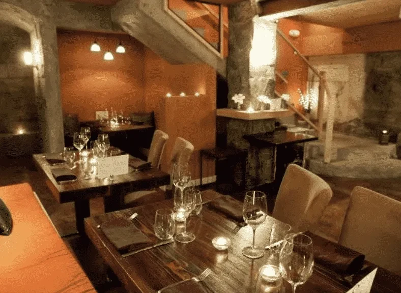 Warm, rustic restaurant dining room with set tables and stone walls.