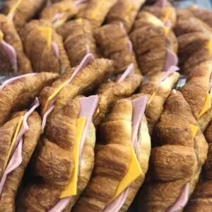 Numerous tightly packed ham and cheese croissant sandwiches.