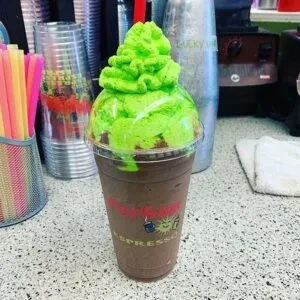 Dark blended drink with bright lime-green whipped cream in a Biggby cup.