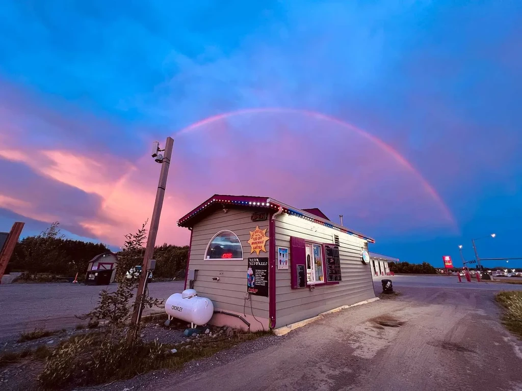 Coffee stand with 'OPEN' sign at dusk under a vibrant rainbow.