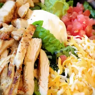 Overhead grilled chicken salad with tomatoes, cheese, lettuce, and creamy dressing.