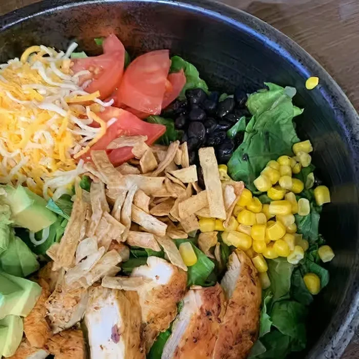 Vibrant chicken salad bowl featuring lettuce, cheese, tomatoes, beans, corn, avocado.