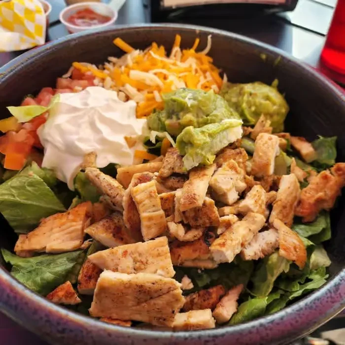 Chicken burrito bowl with lettuce, guacamole, sour cream, and cheese.
