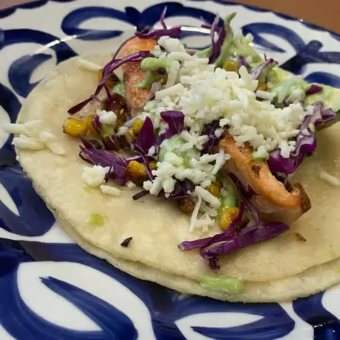Close-up of a taco filled with chicken, purple cabbage, corn, and cheese.
