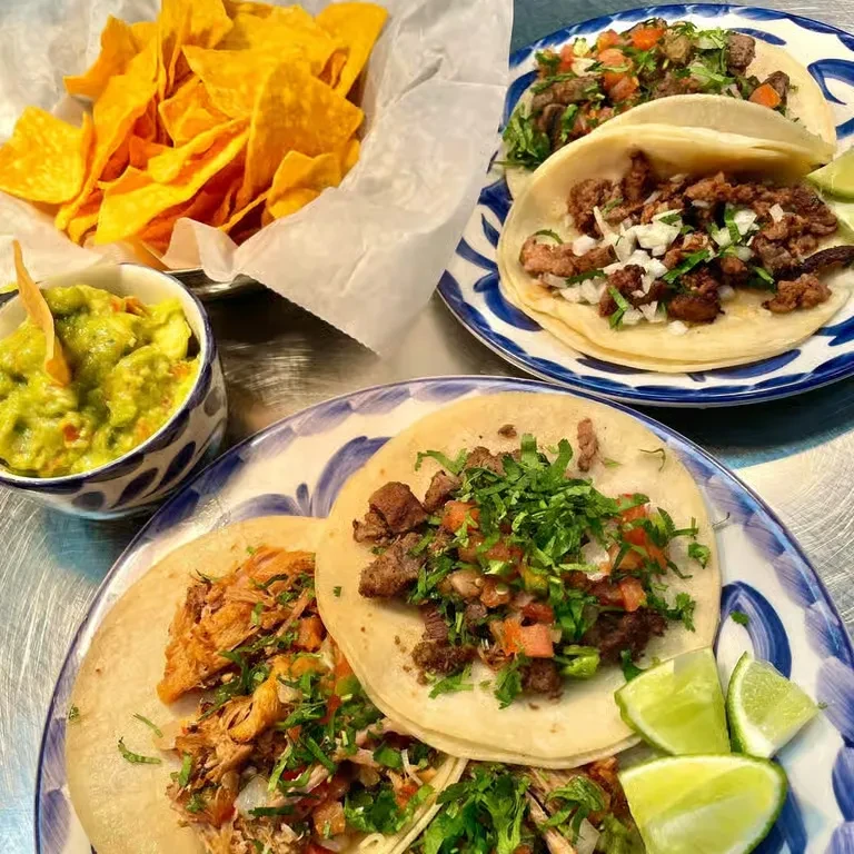 Overhead of Mexican food: tacos, chips, guacamole on metal table.