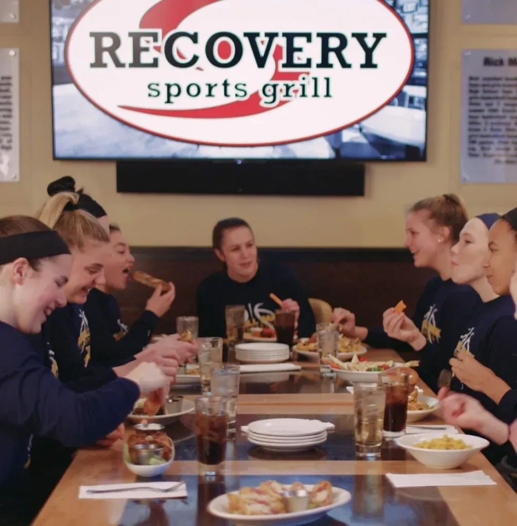 Young women in team shirts dining at Recovery Sports Grill.