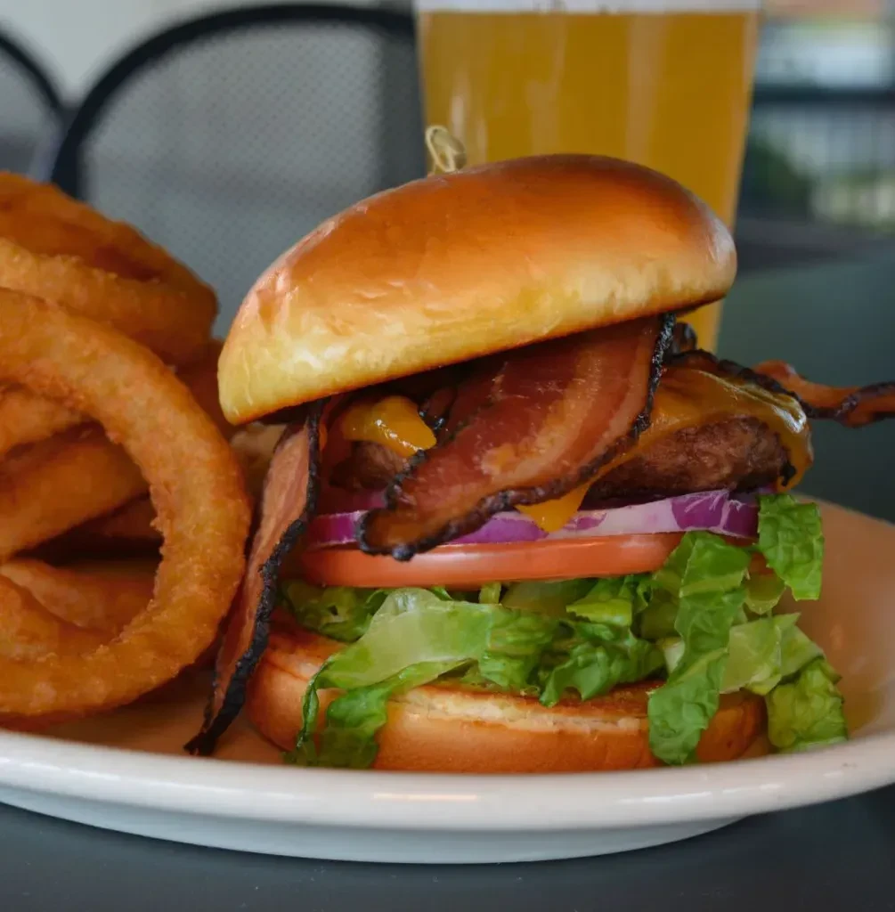 Close-up of a stacked bacon cheeseburger with crispy onion rings.