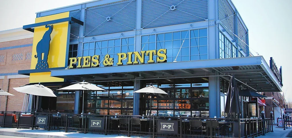 Modern PIES & PINTS restaurant exterior with yellow facade and patio.