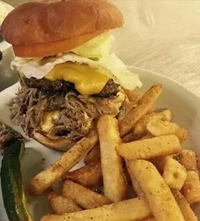 Hearty burger with pulled meat, cheese, fries, and a pickle.