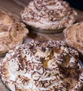 Four individual cream tarts topped with dark chocolate shavings on wood.