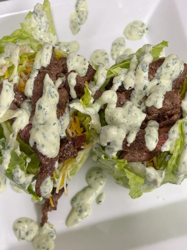 Lettuce cups with beef, cheese, and creamy herb dressing on a white plate.