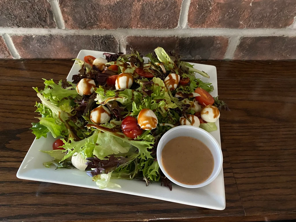 Fresh salad with mixed greens, tomatoes, mozzarella, balsamic, and dressing.