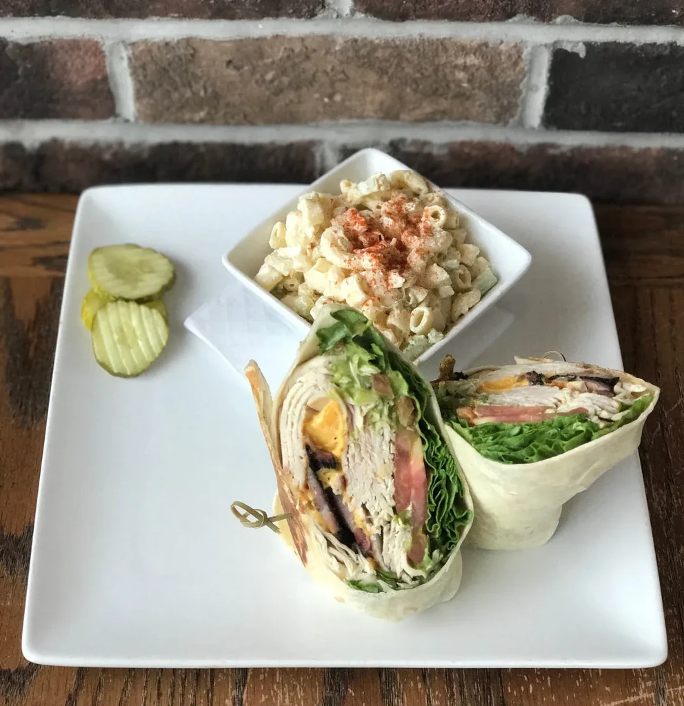 Cut deli wrap, macaroni salad, and pickles on a white plate.