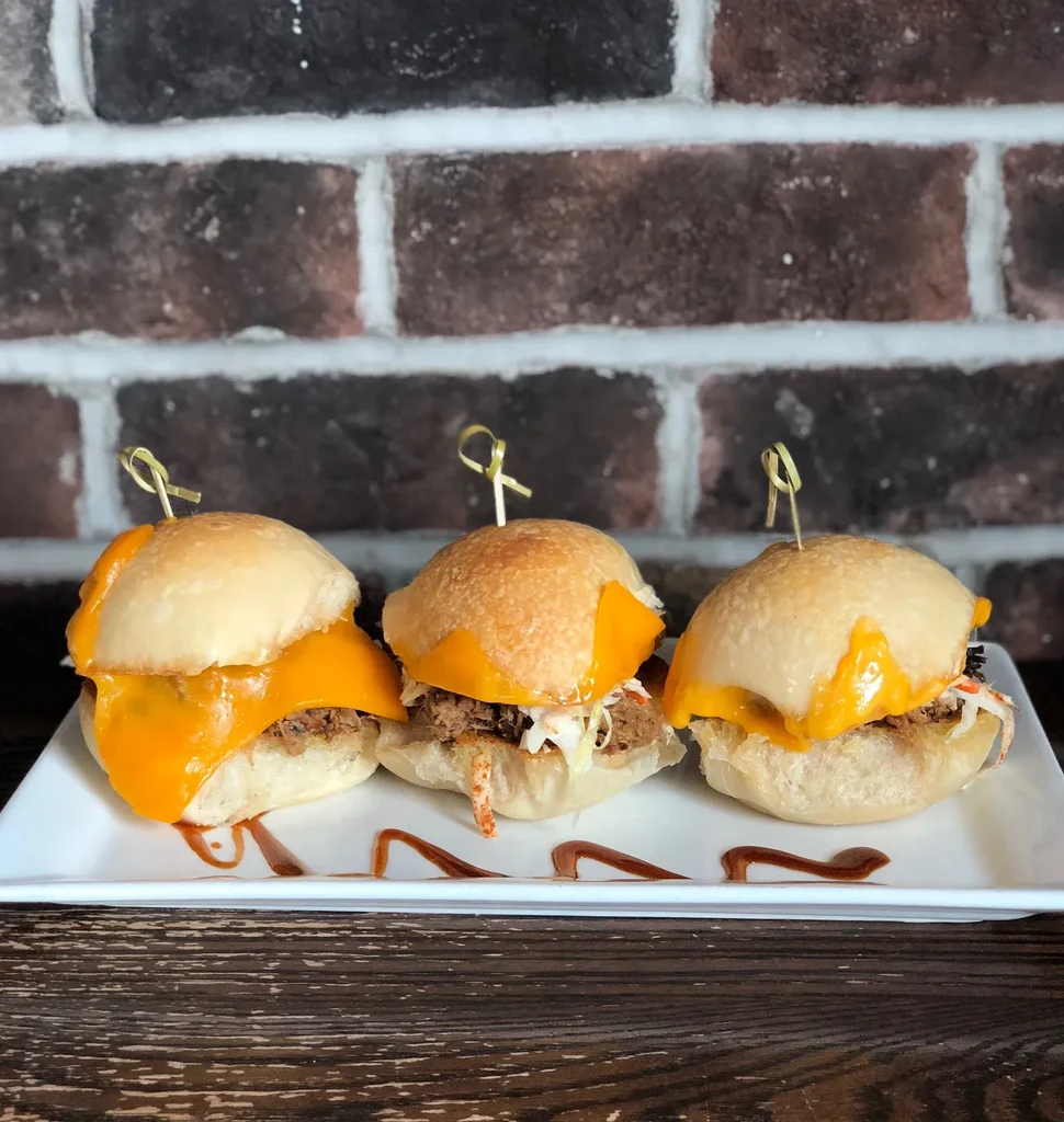 Three pulled meat sliders with coleslaw and melted cheese.