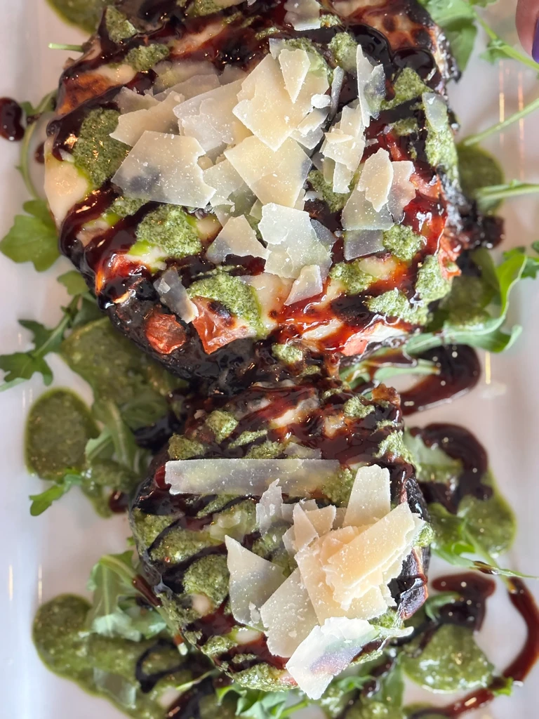 Two dark roasted items topped with pesto, cheese, balsamic, and arugula.