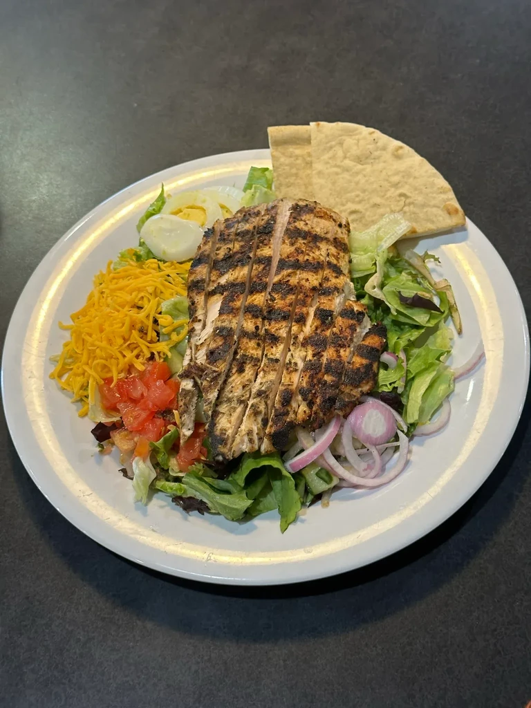 Overhead grilled chicken salad with cheese, tomatoes, egg, and pita.