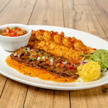 Close-up plate of steak, shrimp, rice, guacamole, and salsa on wood.