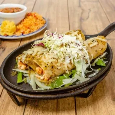 Sizzling platter of cheesy burritos or enchiladas with rice and beans.