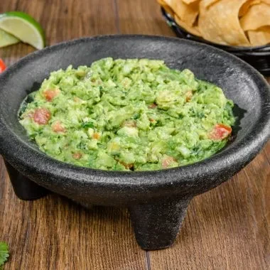 Chunky green guacamole in a black molcajete, with chips and lime.