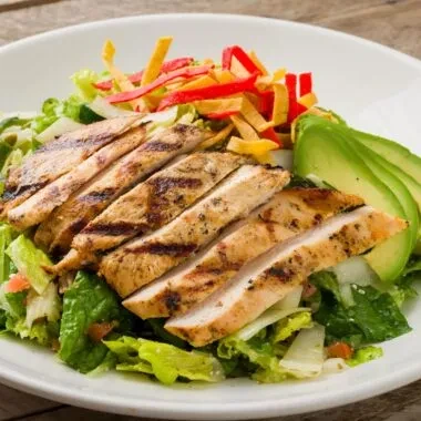 Grilled chicken salad with avocado, mixed greens, and tortilla strips.