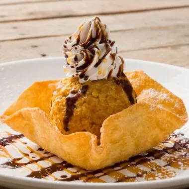 Fried ice cream in crispy bowl with cream, chocolate, powdered sugar.