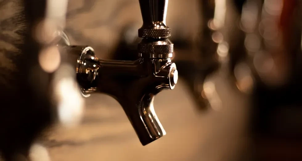 Close-up of a polished chrome beer tap against blurred warm lights.