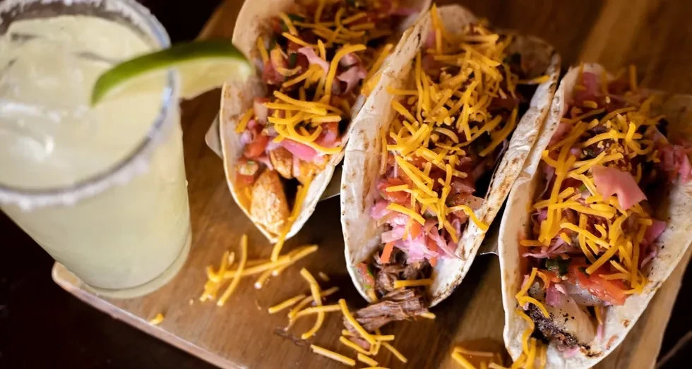 Overhead shot of three loaded tacos and a salt-rimmed margarita.