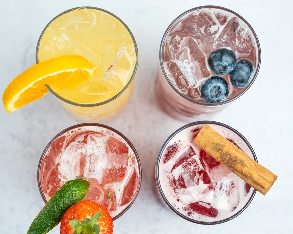 Top-down view: four colorful, garnished iced drinks on a light surface.