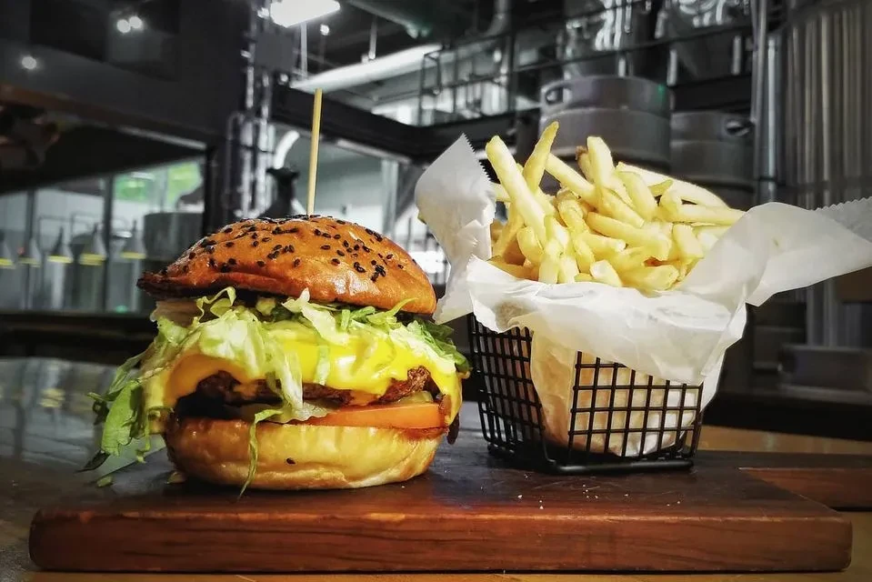 Large burger with melted cheese and fries on a wooden board.