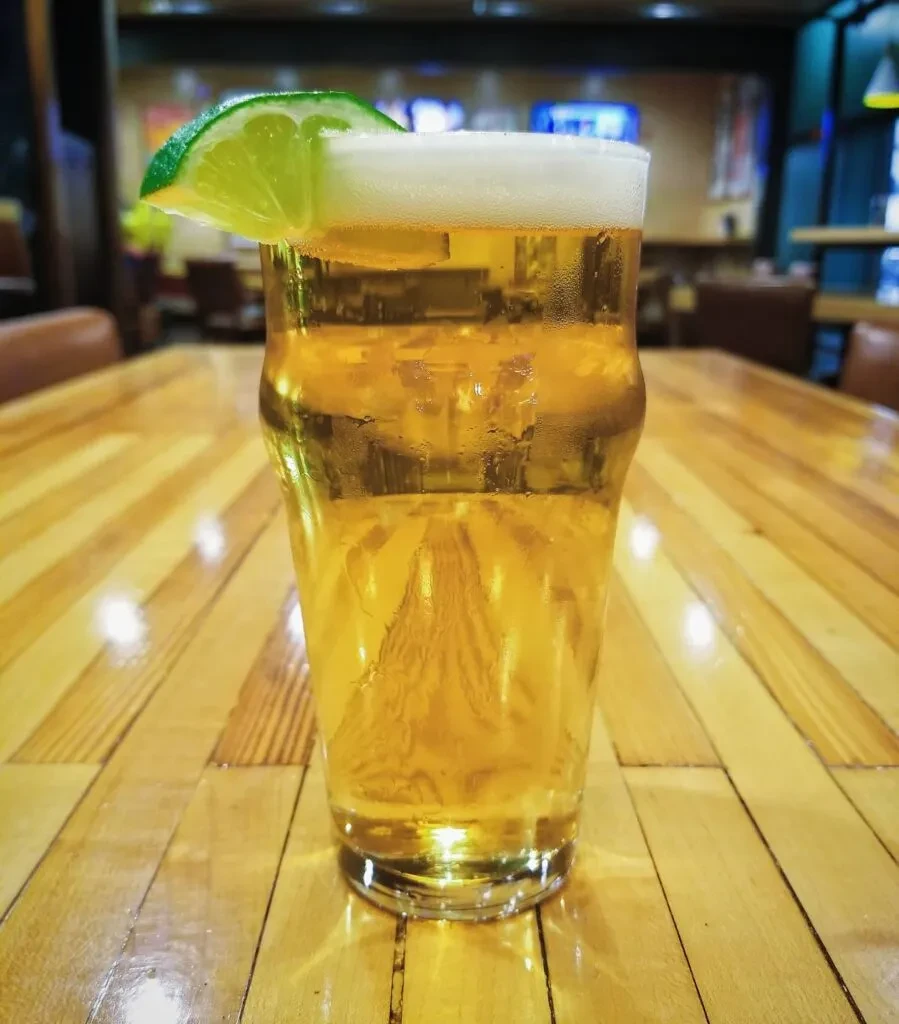 Pint glass of cold beer with lime on a wooden table.